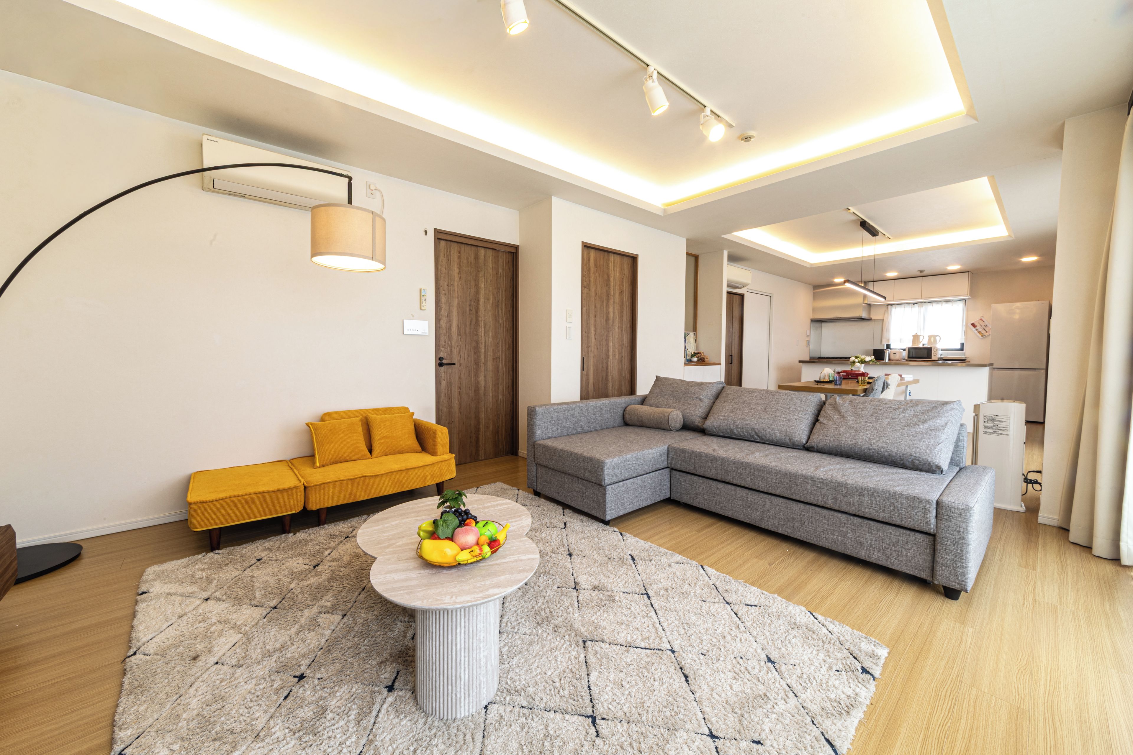 A modern living room with a sectional sofa, a round coffee table with fruit, and a kitchen in the background.