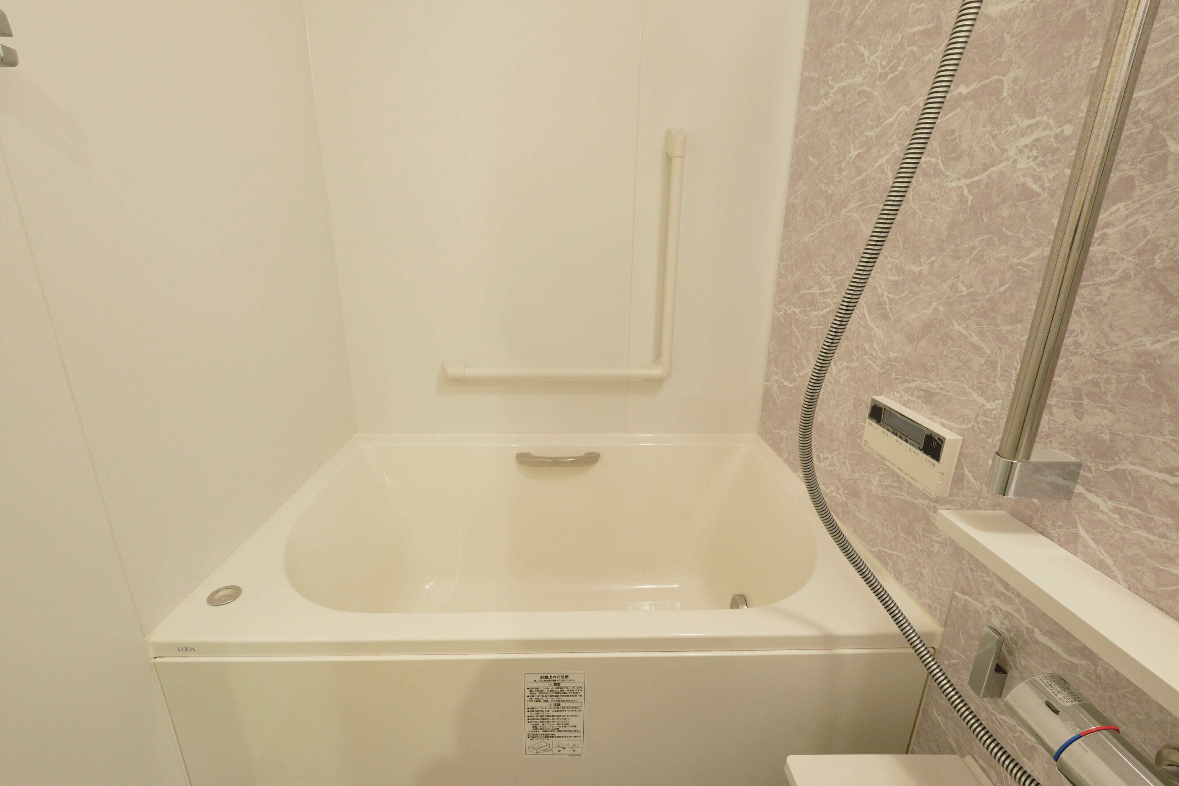 A bathroom with a white bathtub, a handrail, a control panel, and a towel rack.