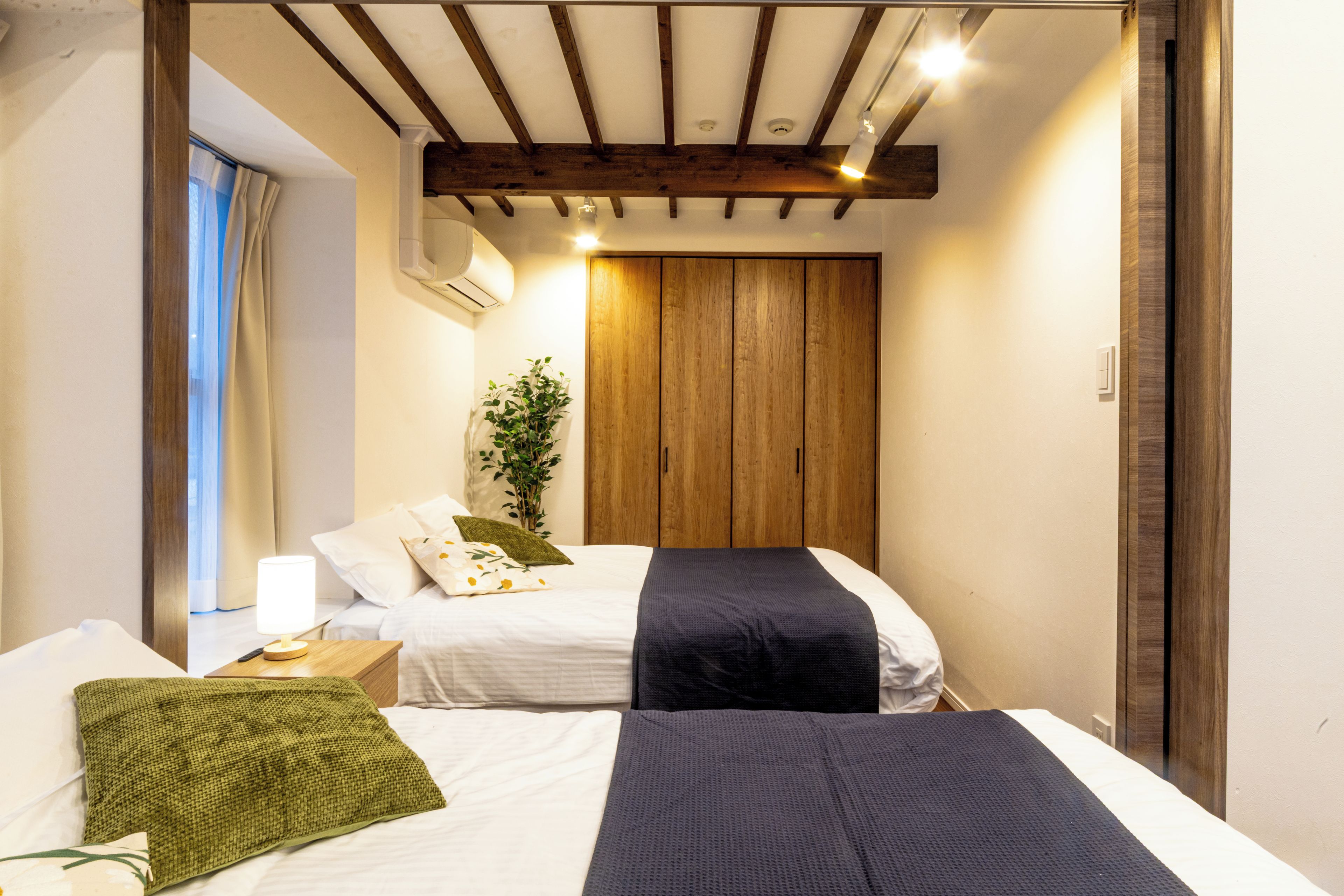 Un dormitorio con dos camas, techo de madera y una planta.