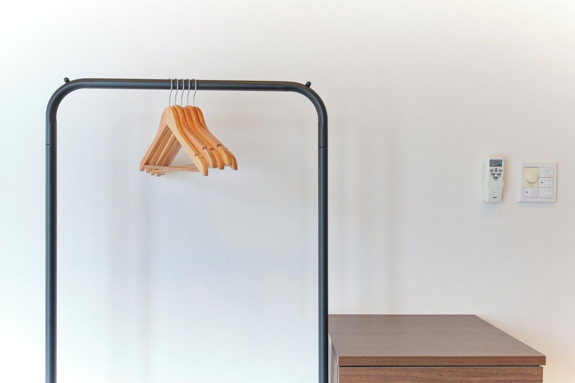 A room with a metal wardrobe, wooden hangers, and a thermostat on the wall.