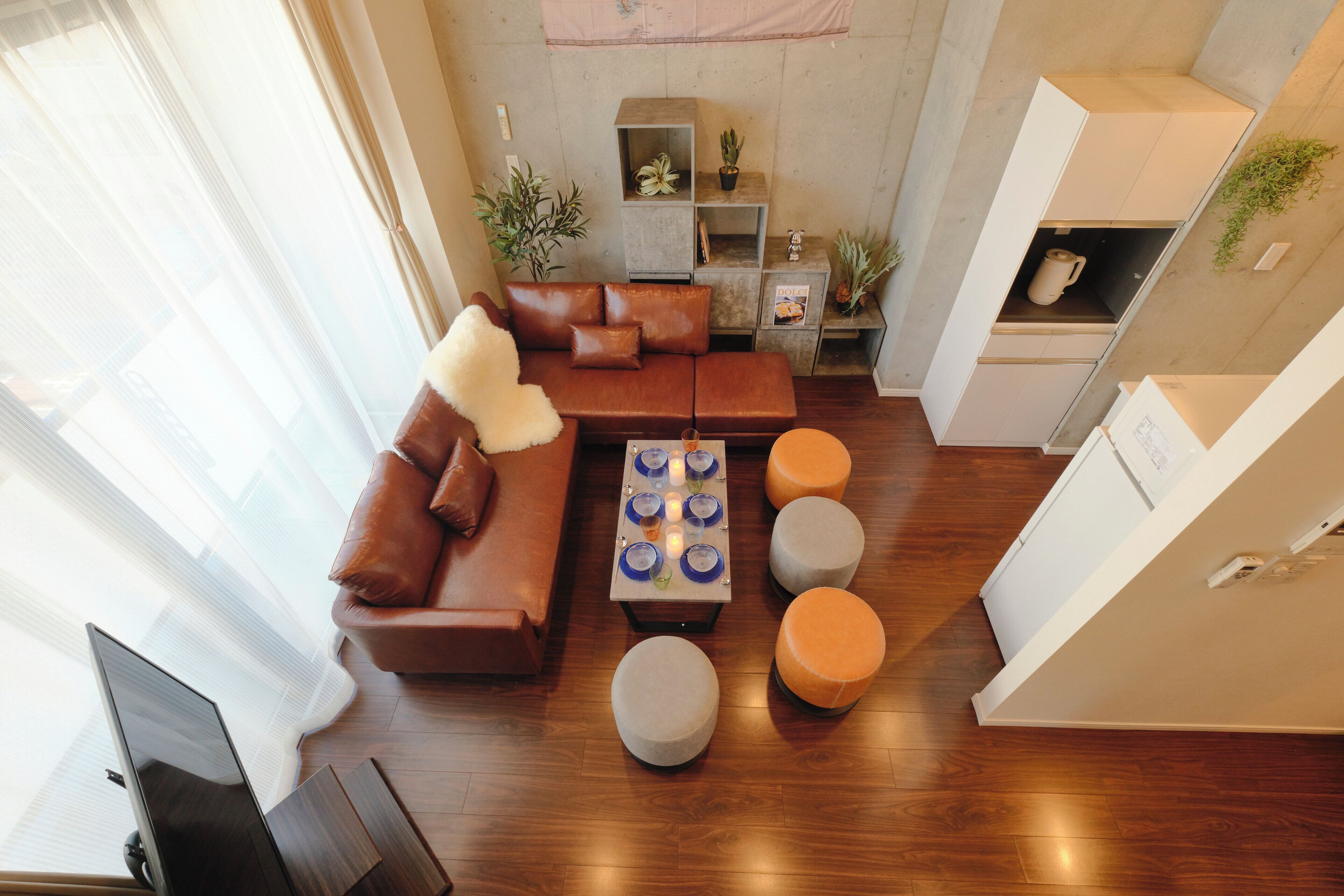 Una sala de estar moderna con un sofá de cuero marrón, una mesa de centro con platos azules y blancos, y otomanas naranjas.