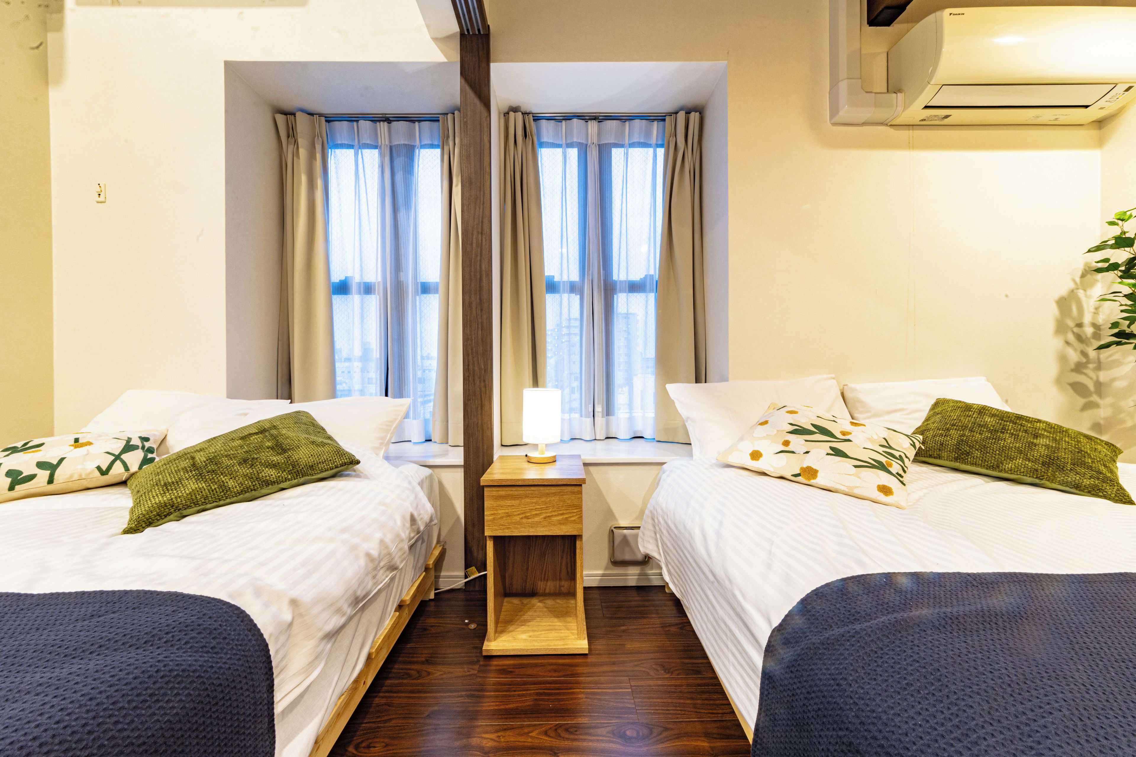 Ein Hotelzimmer mit zwei Betten, einem Nachttisch, einer Lampe und einem Fenster mit Vorhängen.