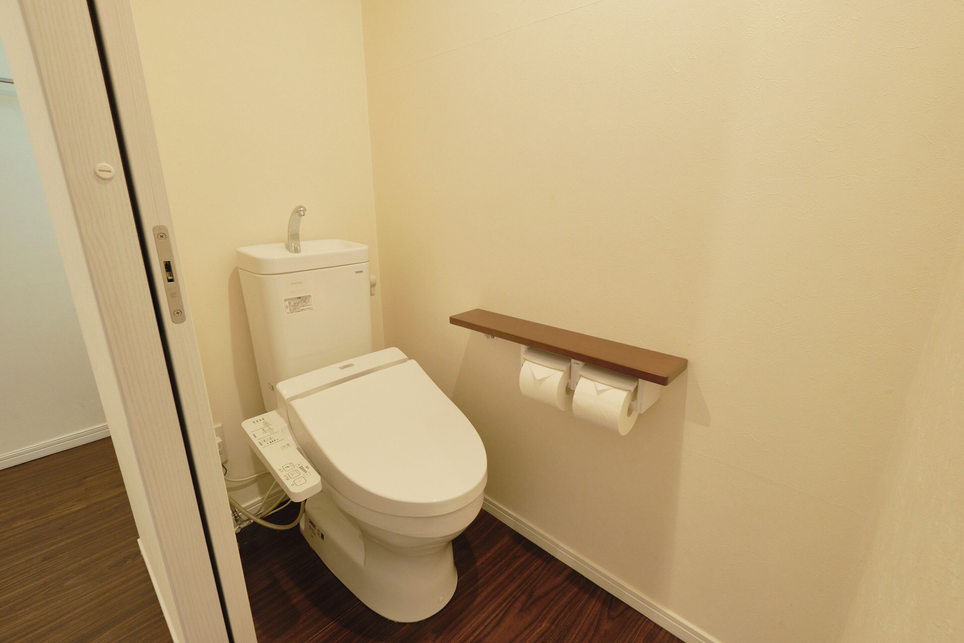 Ein kleines, sauberes Badezimmer mit Toilette, einem hölzernen Ablagefach mit Toilettenpapier und einer weißen Wand.