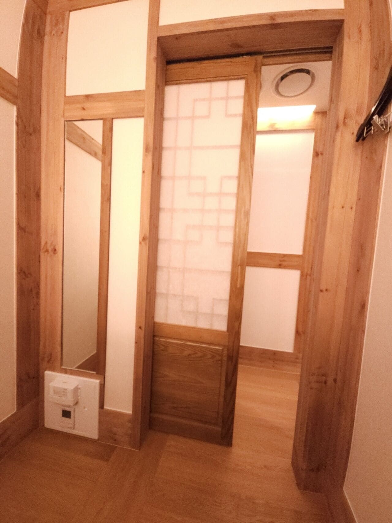 Un couloir étroit avec des poutres en bois et une porte en verre dépoli.