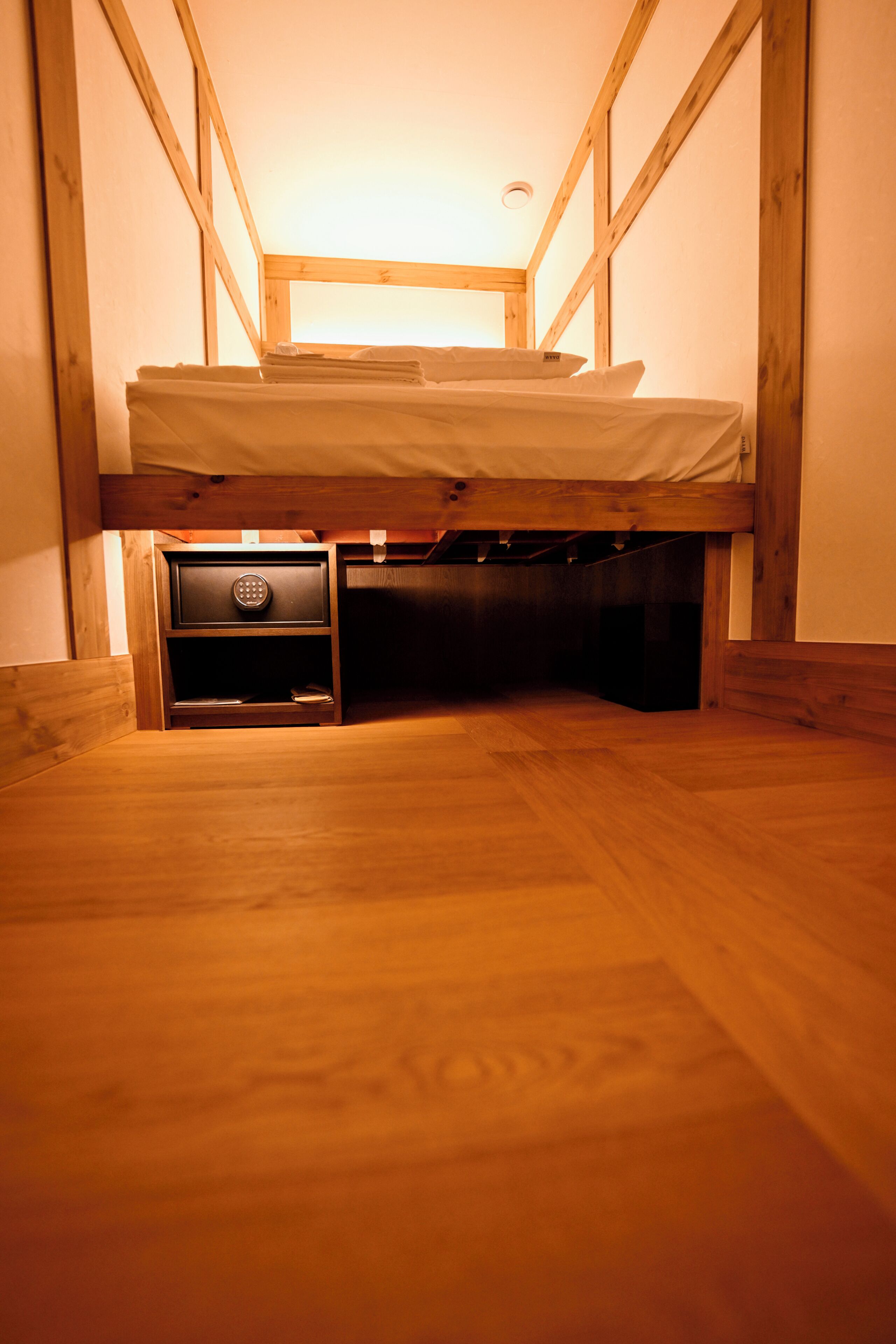 A narrow room with a bunk bed, a small drawer unit, and wooden walls.
