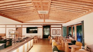 Un interior amplio con vigas de madera en el techo, una zona de bar con taburetes y un área de estar con mesas y sillas.
