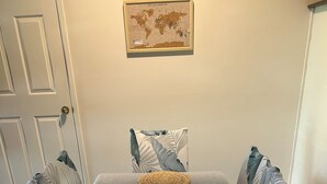 A dining area with a table set for four, featuring woven placemats, a bowl of fruit, and a framed world map on the wall.