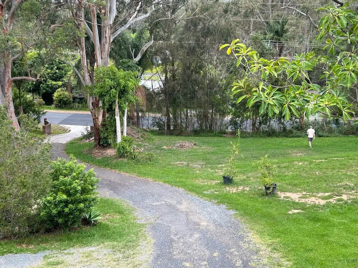 Uma trilha serpenteia por uma área gramada com árvores, e uma pessoa caminhando ao longe.