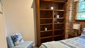 Een slaapkamer met een bed, een houten boekenkast, een stoel en een raam met uitzicht.