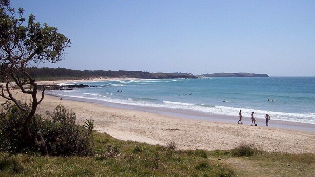 A beach with a sandy shore, ocean waves, and a few people walking.