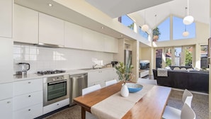 A modern kitchen with white cabinetry, a dining area with a wooden table and chairs, and a large window providing natural light. - Gorgeous 2-Bed Victorian Home in Artsy Suburb (Brunswick)