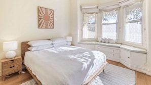 A bedroom with a bed, bedside tables, a window seat, and a wall-mounted artwork. - Gorgeous 2-Bed Victorian Home in Artsy Suburb (Brunswick)
