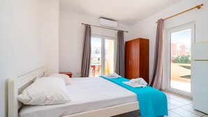 Hotellihuone, jossa on sänky, vaatekaappi, työpöytä ja ikkuna, jossa on verhot.