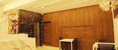 A modern reception area with a marble reception desk, a wooden wall panel, and a seating area with two chairs and a table.