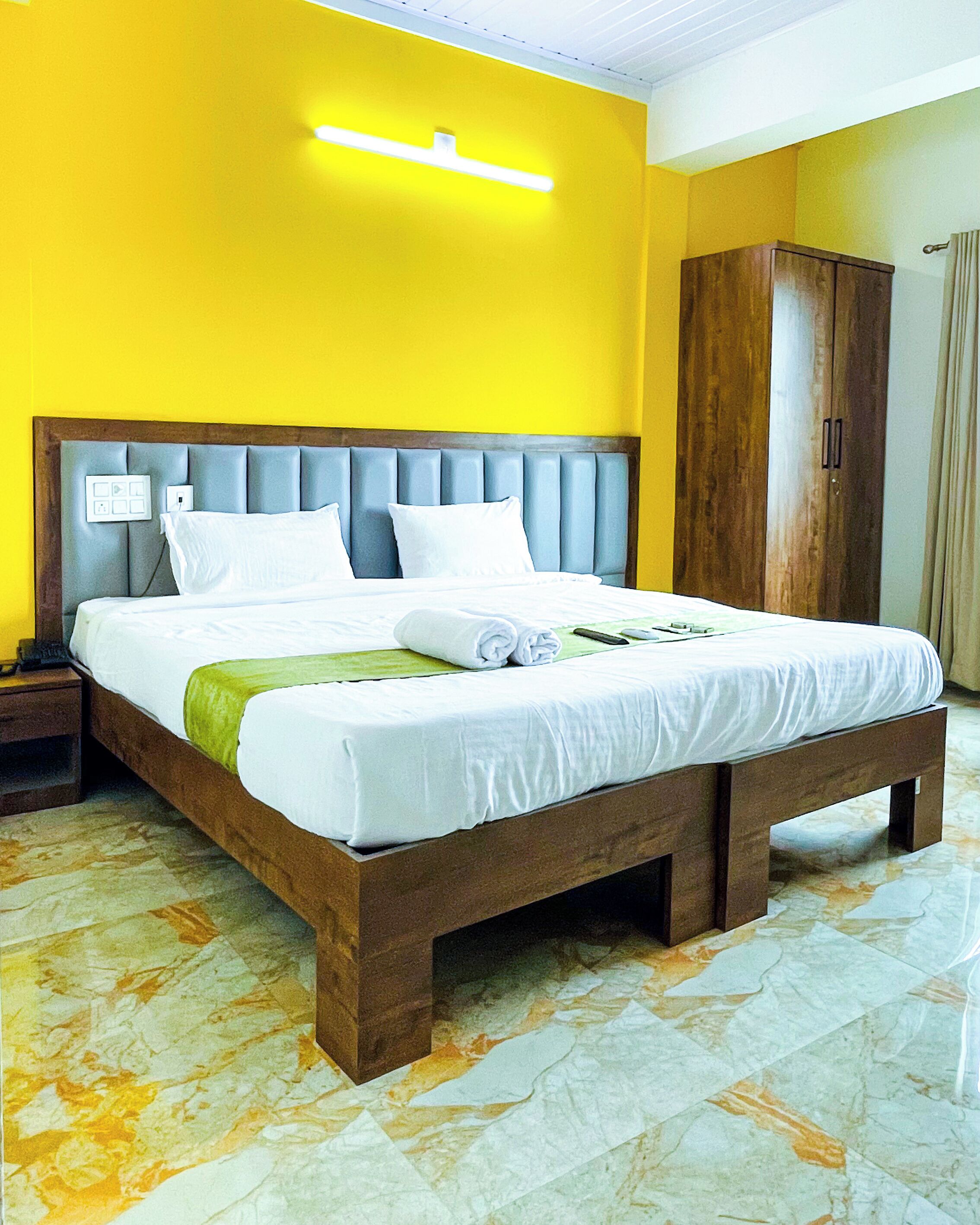 A neatly made bed with white linens, a wooden headboard, and a green towel.