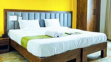 A neatly made bed with white linens, a wooden headboard, and a green towel.