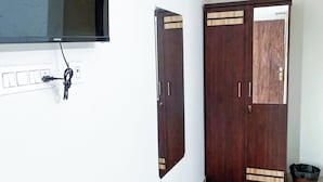 Una habitación con una televisión montada en la pared, un armario de madera con dos puertas, un suelo con diseño de mármol y un cesto de basura.