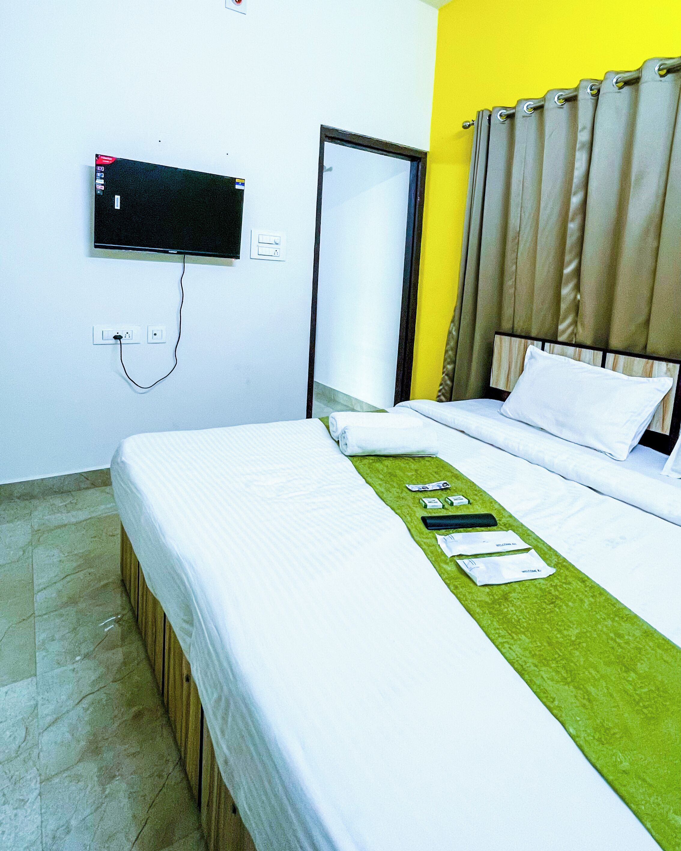 A hotel room with a bed, a television mounted on the wall, a window with curtains, and a door.