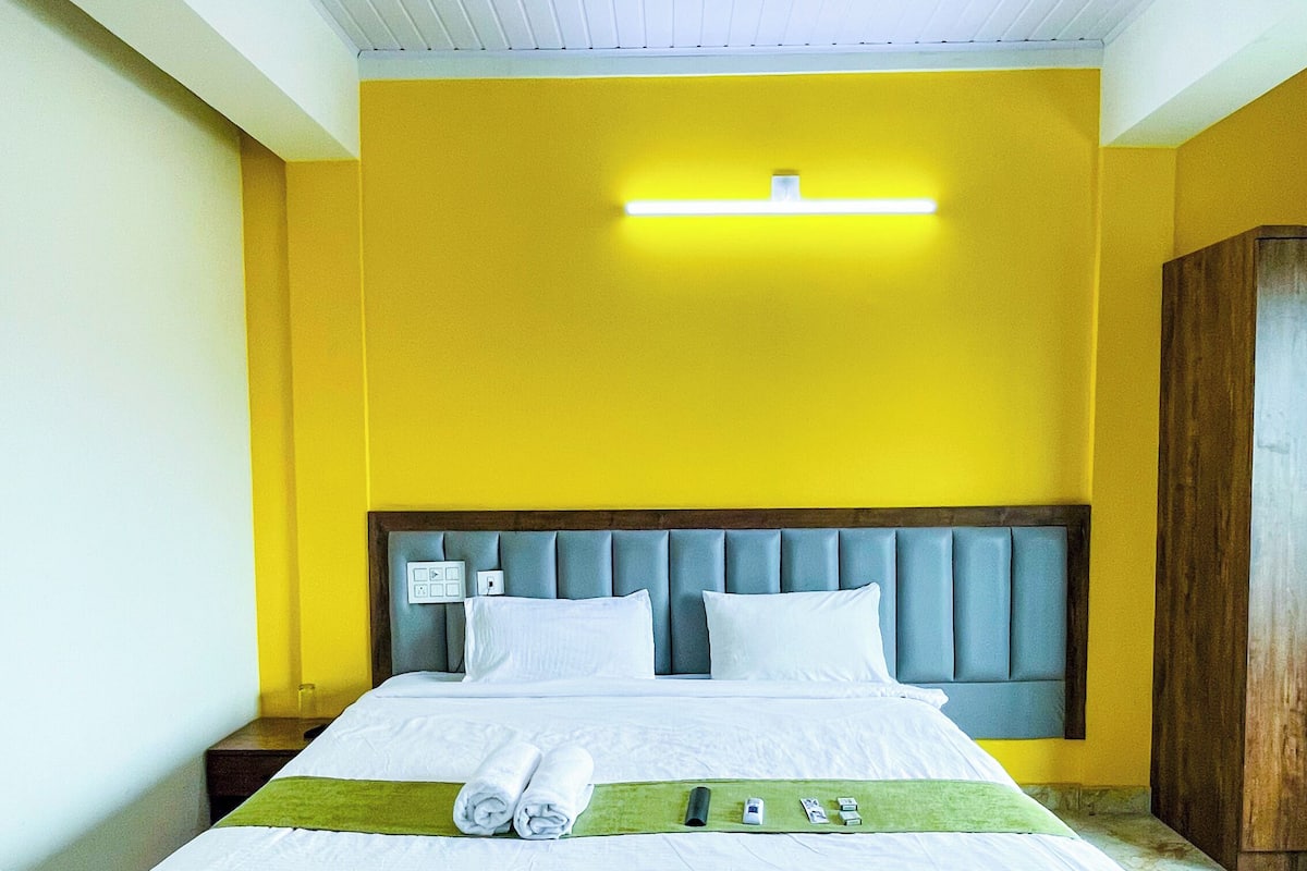 A neatly made bed with white linens, a wooden headboard, and a green towel on the side.