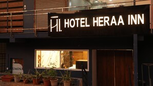 Un letrero de hotel con el nombre "HI. HOTEL HERAA INN" y una ventana que muestra una vista del interior.
