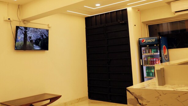 Un interior moderno con piso de mármol, un banco de madera, televisor de pantalla plana, una puerta negra y un refrigerador Pepsi.