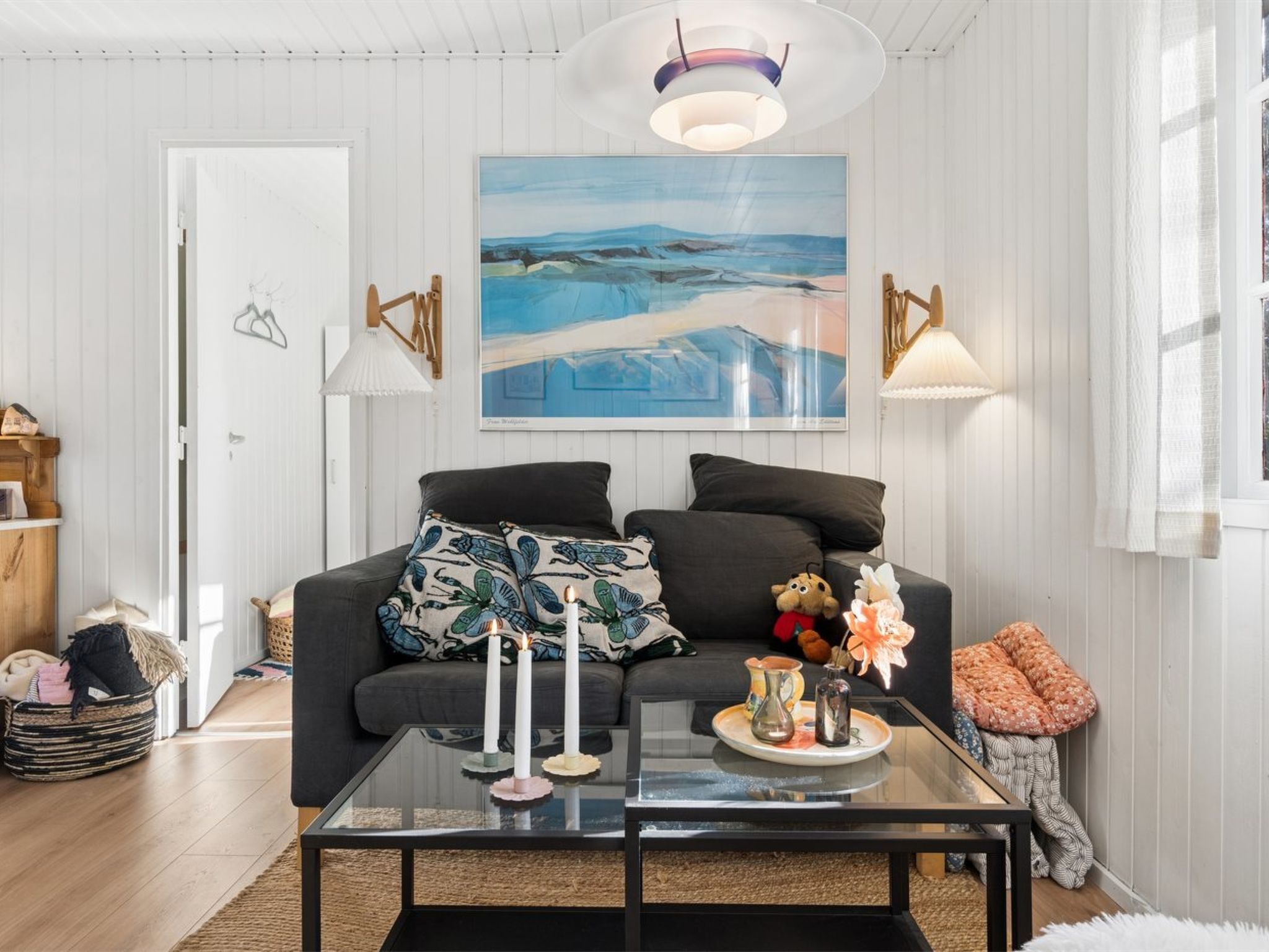 A modern living room with a sofa, a glass coffee table, and a painting above it.