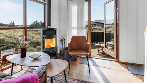 Una habitación acogedora con estufa de leña, ventanas amplias, zona de comedor y vistas al exterior.