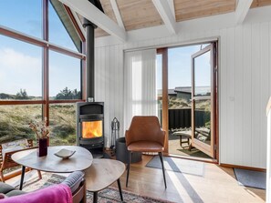 Una habitación acogedora con estufa de leña, ventanas amplias, zona de comedor y vistas al exterior.