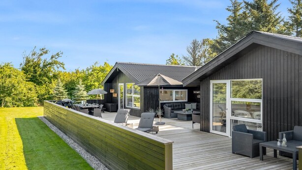 Een modern terras buiten met houten vloer, omgeven door een houten schutting en een gazon.