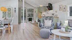 Een ruime woonkamer met een eettafel, een bank en een salontafel. Er is een keuken met kastjes en een raam.