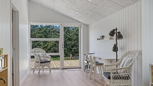 Ruime kamer met een grote glazen schuifdeur die leidt naar een terras. Er staan wicker-stoelen en een tafel met een lamp.