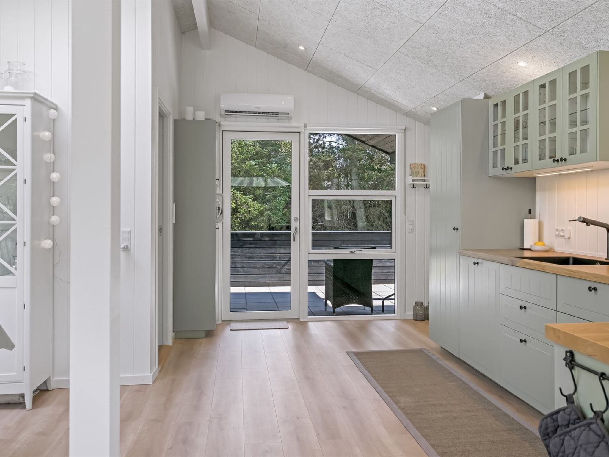 A modern kitchen with white cabinetry, a wooden countertop, and a large sliding glass door leading to an outdoor area.