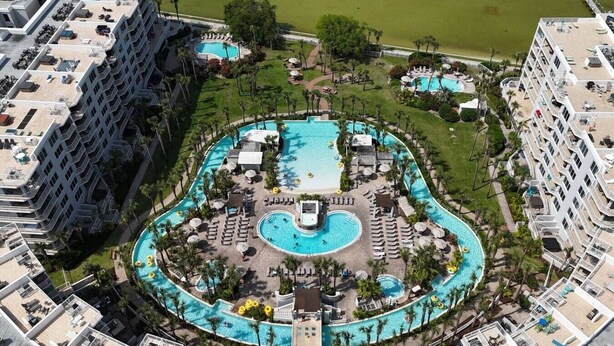 Vue aérienne d’un hôtel doté de plusieurs piscines, d’une plage et d’une grande pelouse.