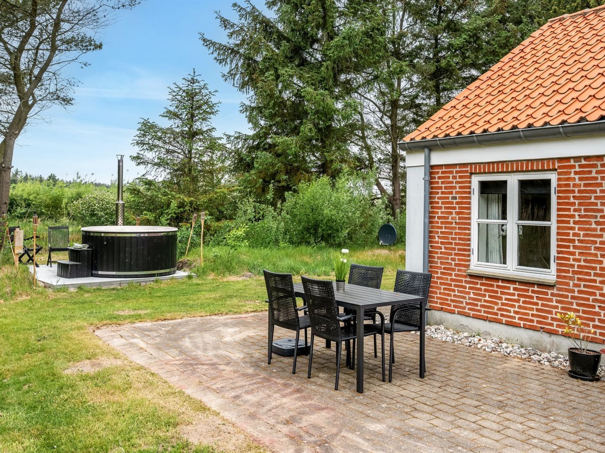 A patio with a table and chairs, a hot tub, and a brick building with a window.