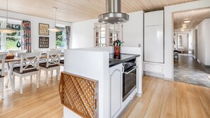 Una cocina moderna con horno empotrado, campana extractora de acero inoxidable y un comedor con sillas blancas y una mesa de madera.