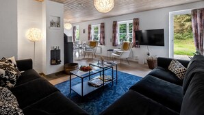 Una sala de estar moderna con un sofá negro, una mesa de centro y un televisor montado en la pared. Hay dos sillones y una chimenea.