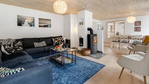 Una sala de estar moderna con un sofá negro, una mesa de centro y una alfombra azul. Se observa una chimenea y un área de comedor al fondo.