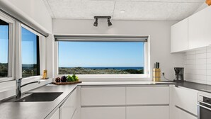 A modern kitchen with white cabinetry, a large window with a view of the sea, and a built-in oven.