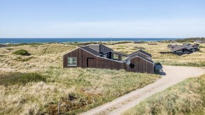 A coastal area with modern wooden houses, a dirt path, and a clear view of the sea.