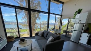 Un salon moderne avec un canapé, une table basse et une vue sur un lac, grâce à de grandes fenêtres.