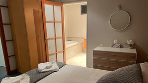 Une chambre d’hôtel avec un lit, une armoire en bois, une commode, un miroir et une salle de bain visible à travers une porte ouverte.