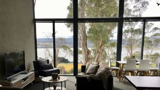 Un salon moderne doté d’une grande fenêtre, d’un téléviseur à écran plat, d’un canapé, d’une table basse et d’un coin repas avec des chaises.