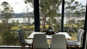 Un espace repas comprenant une table et des chaises, donnant sur un paysage pittoresque avec des arbres et une étendue d’eau.