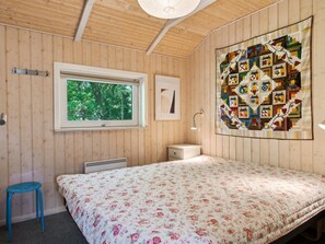 Relax in a serene bedroom with a large window offering a view of lush greenery, a comfortable bed, and a cozy quilt.