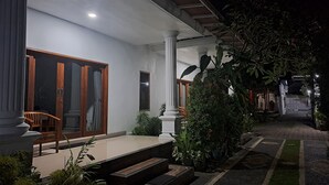 A well-lit entrance with a porch, steps leading up to the door, and a garden area with potted plants. - srinadi guest house (Buleleng)