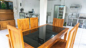 A dining area with a glass-top table and wooden chairs. - srinadi guest house (Buleleng)