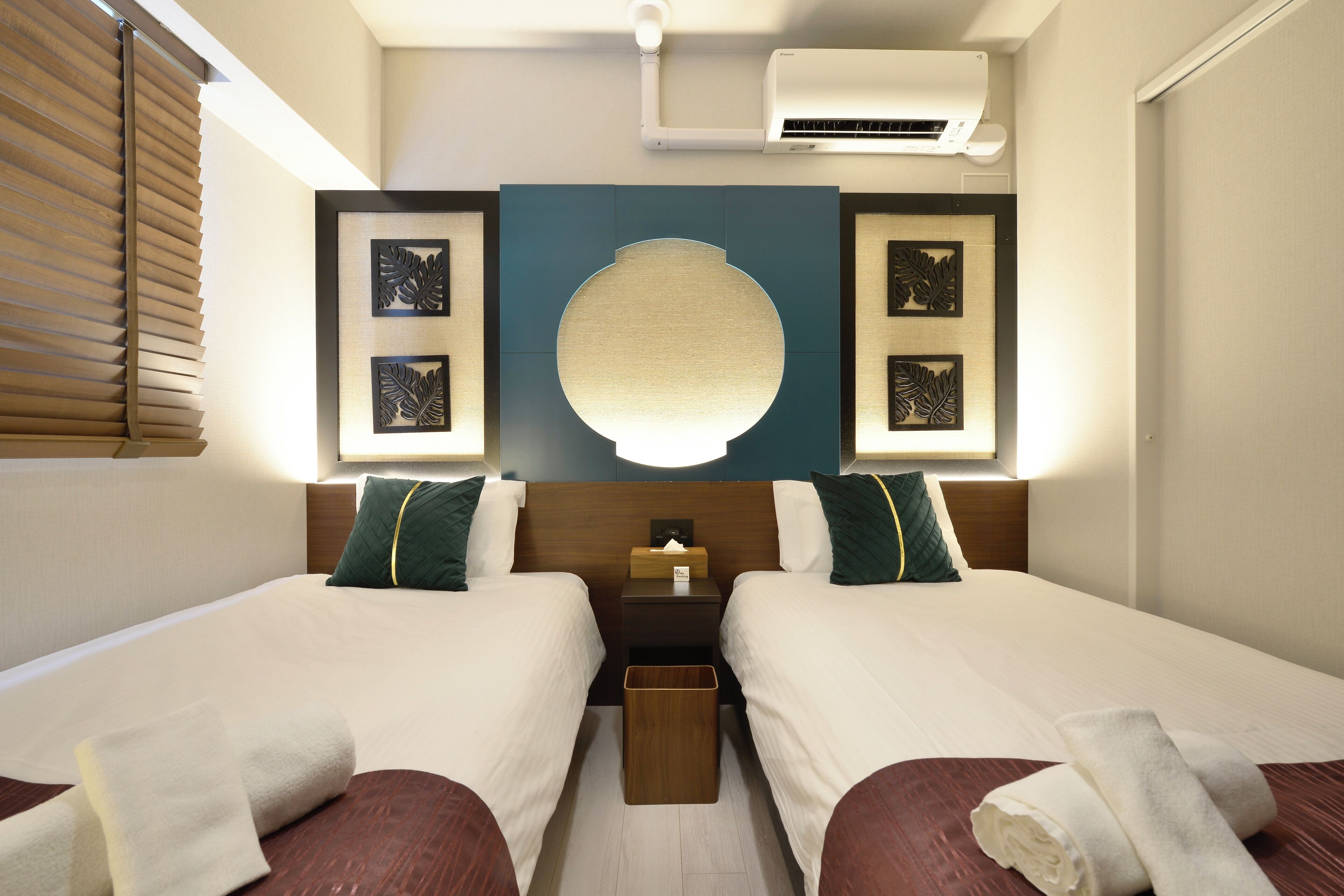 Una habitación de hotel con dos camas, una mesita de noche, un equipo de aire acondicionado y decoración en la pared.