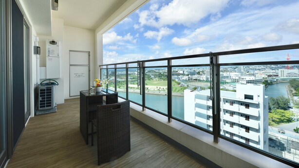 A balcony with a view of a river and buildings, a small table with chairs, and a window with a view of the city. - Branchera naha akebono premist R78 (Naha)