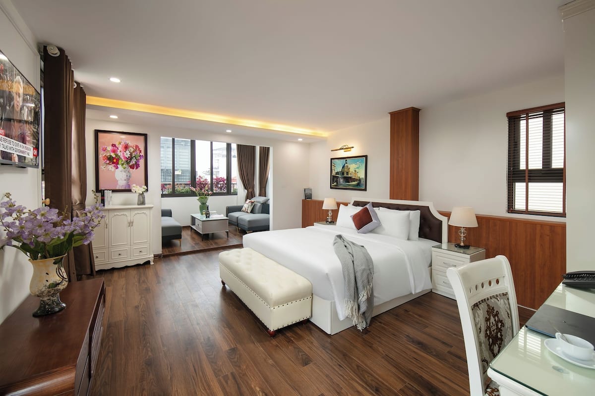 A modern hotel room with a large bed, a desk, a chair, a small table, and a sofa.