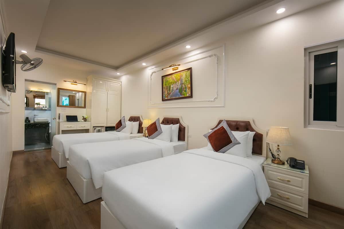 A hotel room with three beds, a desk, a mirror, a painting, and a TV.